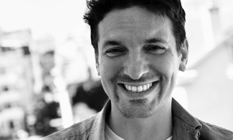 Le 6 octobre, Cartoon Network et HBO Max lanceront «Le Monde Merveilleusement Bizarre de Gumball», une nouvelle série animée produite par Hanna-Barbera Studios Europe, le studio d’animation européen de Warner Bros. Discovery. Composée de 19 épisodes de 11 minutes, la série marque le grand retour d’un univers diffusé dans près de 190 pays et traduit dans plus de 30 langues. Son créateur, Ben BOCQUELET, revient sur la genèse de cette suite, ses choix artistiques et ses ambitions pour Gumball, entre innovations visuelles, humour universel et projet de long-métrage toujours en discussion. «Gumball» revient après sept ans d’absence. Faut-il parler d’une suite, d’un reboot ou d’un renouveau ? Je vois cette saison comme une continuité. À l’origine, nous travaillions sur un long-métrage prévu avant cette série, mais le projet a été temporairement retardé. Entre-temps, la saison a été validée. Sept années se sont écoulées, le monde et notre audience ont évolué : nous nous sommes donc demandé ce que signifie être un enfant en 2025, dans un contexte marqué par les réseaux sociaux, l’IA ou encore une certaine anxiété face à l’avenir. C’est tout cela que nous avons voulu injecter dans le «Gumball» d’aujourd’hui. Comment résumer le processus de fabrication d’un épisode ? Chaque épisode suit une véritable gestation de neuf mois. Tout commence par le storyboard, qui fixe le rythme et l’efficacité des blagues. Puis vient l’animatique, qui nous permet de vérifier que l’épisode «tient» en 11 minutes. Les voix sont enregistrées très tôt, ce qui sert de base aux animateurs. Le layout assure la cohérence visuelle entre les différents éléments. Les décors, réalisés en «photobashing», demandent un gros travail de lumière et de texture. Ensuite vient l’animation, puis la musique – souvent symphonique – qui rythme fortement l’épisode. Enfin, le compositing intègre les personnages aux décors, ajoute les effets de caméra et scelle l’illusion. Au total, deux ans sont nécessaires pour produire une saison complète. Comment cet univers a-t-il vu le jour ? À l’époque, je travaillais dans la publicité à Londres. Je créais sans cesse des personnages pour des pitchs qui, souvent, n’aboutissaient pas. Je les ai «recyclés» dans une idée de sitcom centrée sur la maison et l’école. Un T-Rex est devenu le bully, le nerd un robot… C’est ainsi qu’est né «Gumball», quand Cartoon Network a validé cette orientation plus proche des préoccupations des enfants. Quelles nouveautés propose cette nouvelle saison sur Cartoon Network et HBO Max ? Nous avons profité de ce retour pour redessiner le logo et réinventer la séquence d’introduction avec l’artiste Jack Sachs. Une séquence a été confiée au graffeur Neck Face, figure de la scène skate de Los Angeles, et notre nouveau showrunner, Matt Layzell, a lui-même réalisé une scène façon cinématique PlayStation 2. Fidèle à son esprit de laboratoire visuel, «Gumball» reste un terrain d’expérimentation graphique permanent. La tonalité «tous publics» qui a fait le succès de la série reste votre boussole ? Absolument. L’idée est que chacun y trouve son compte : l’enfant rit d’une blague visuelle, l’adulte d’un sous-texte ou d’un dialogue. Nous partons souvent d’un postulat absurde et simple puis nous poussons le concept jusqu’à l’extrême. L’univers de «Gumball» s’est aussi nourri d’Internet, en produisant lui-même une multitude de mèmes. Que la série circule ainsi dans l’inconscient collectif me réjouit. Quelle est votre position sur l’intelligence artificielle appliquée à l’animation ? Je la considère comme un outil, à la manière d’un synthétiseur. Par curiosité – et paresse – j’ai demandé à une IA de générer un épisode : c’était médiocre. L’art naît de l’émotion et de l’expérience humaine, choses que l’IA ne peut restituer. Mais si elle permet de soulager les tâches les plus répétitives de l’animation et de redonner du temps aux artistes, alors je pense qu’elle peut trouver sa place. La série est diffusée dans près de 190 pays et traduite dans une trentaine de langues. Comment trouver un humour universel ? En diversifiant les registres. Nous alternons des blagues purement visuelles et cartoonesques, des situations enracinées dans la personnalité des personnages, et des blagues plus allégoriques, souvent adressées aux adultes. Ce mélange garantit que chacun, quel que soit son âge ou sa culture, trouve quelque chose qui lui parle. Où en est le projet de long-métrage «Gumball» ? Il avance. J’ai un nouvel angle narratif, une nouvelle histoire. Tout dépend désormais de la volonté des studios et, surtout, du public. Le meilleur soutien reste de regarder massivement la série. Les studios redoutent l’échec financier, notamment en streaming, mais l’engouement des spectateurs peut accélérer les choses. J’espère que ce film se concrétisera bientôt.